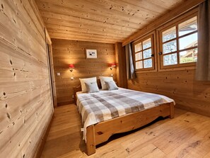 A wooden cabin room with a bed, two wall-mounted lamps, and a window with curtains. - New Listing (Les Allues)