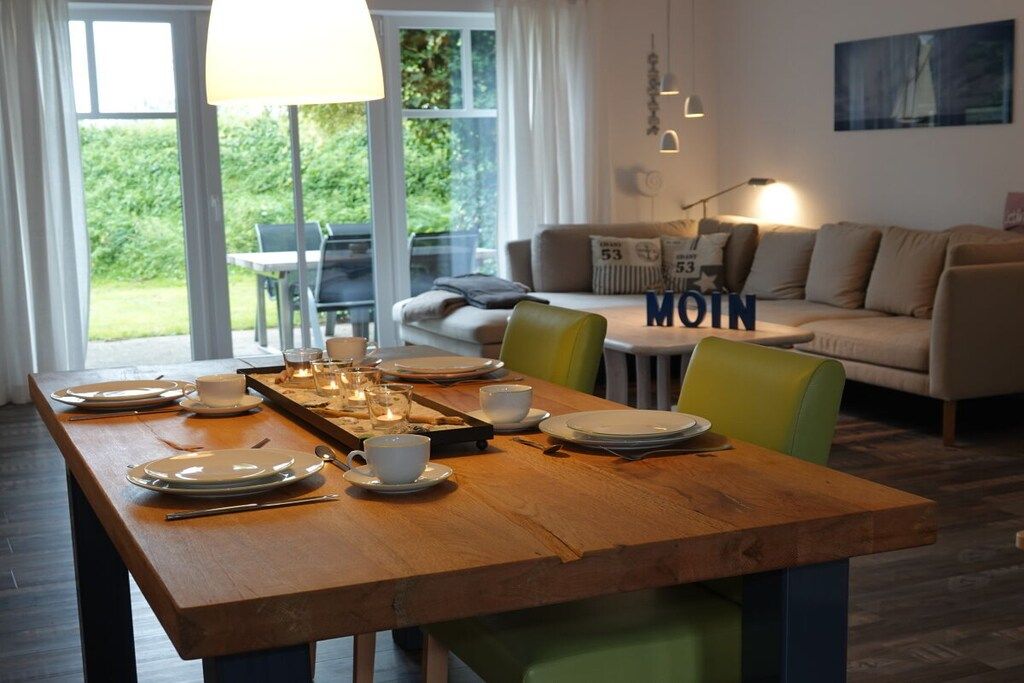 A dining area with a wooden table set for four, a sofa, and a view of the outdoors.