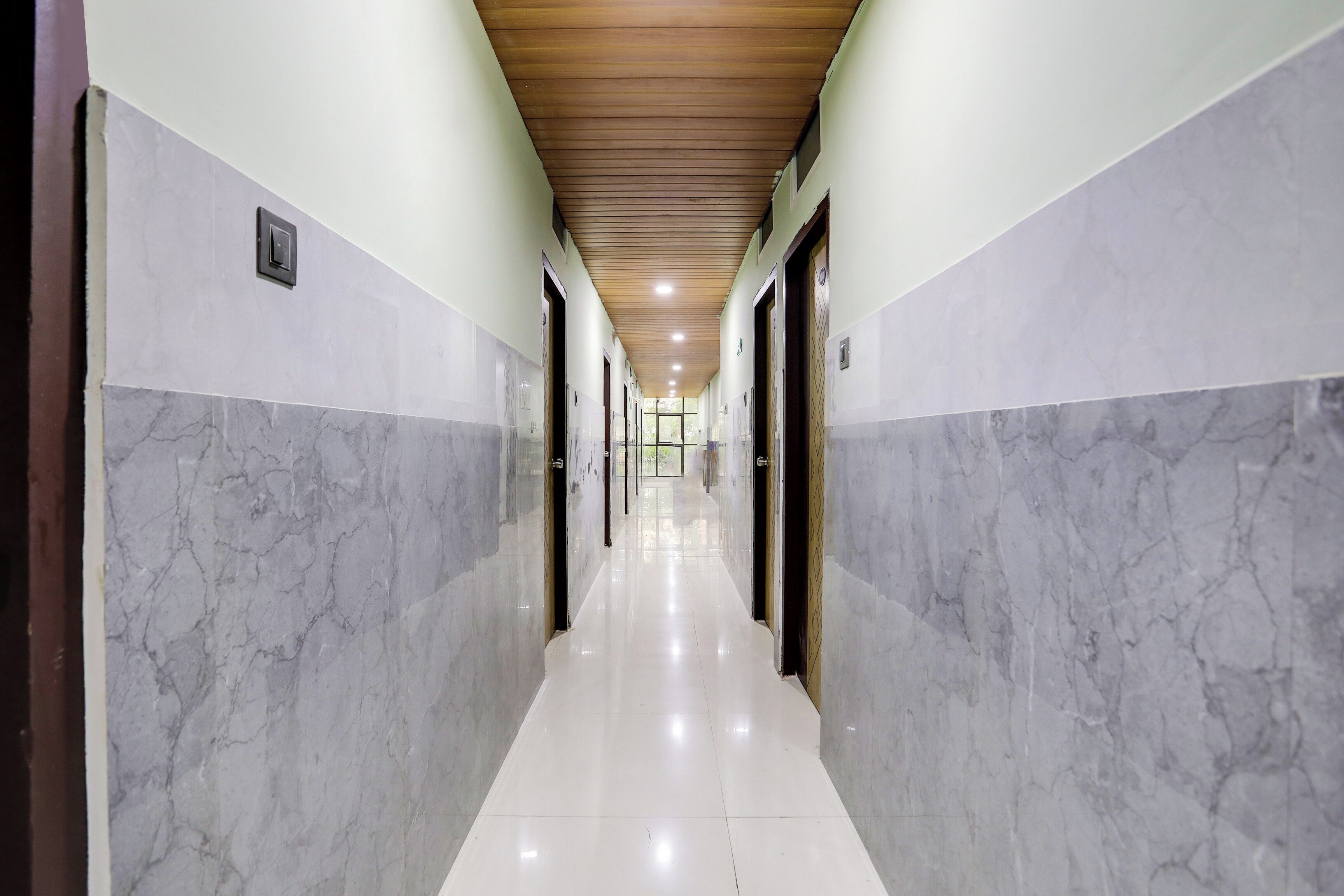 Un pasillo con paredes de mármol y techo de madera, que conduce a una habitación luminosa con ventana.