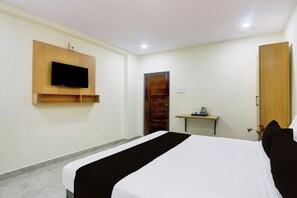 A hotel room with a bed, a TV mounted on the wall, a wooden door, and a small table with a kettle. - Townhouse Kukatpally (Hyderabad)