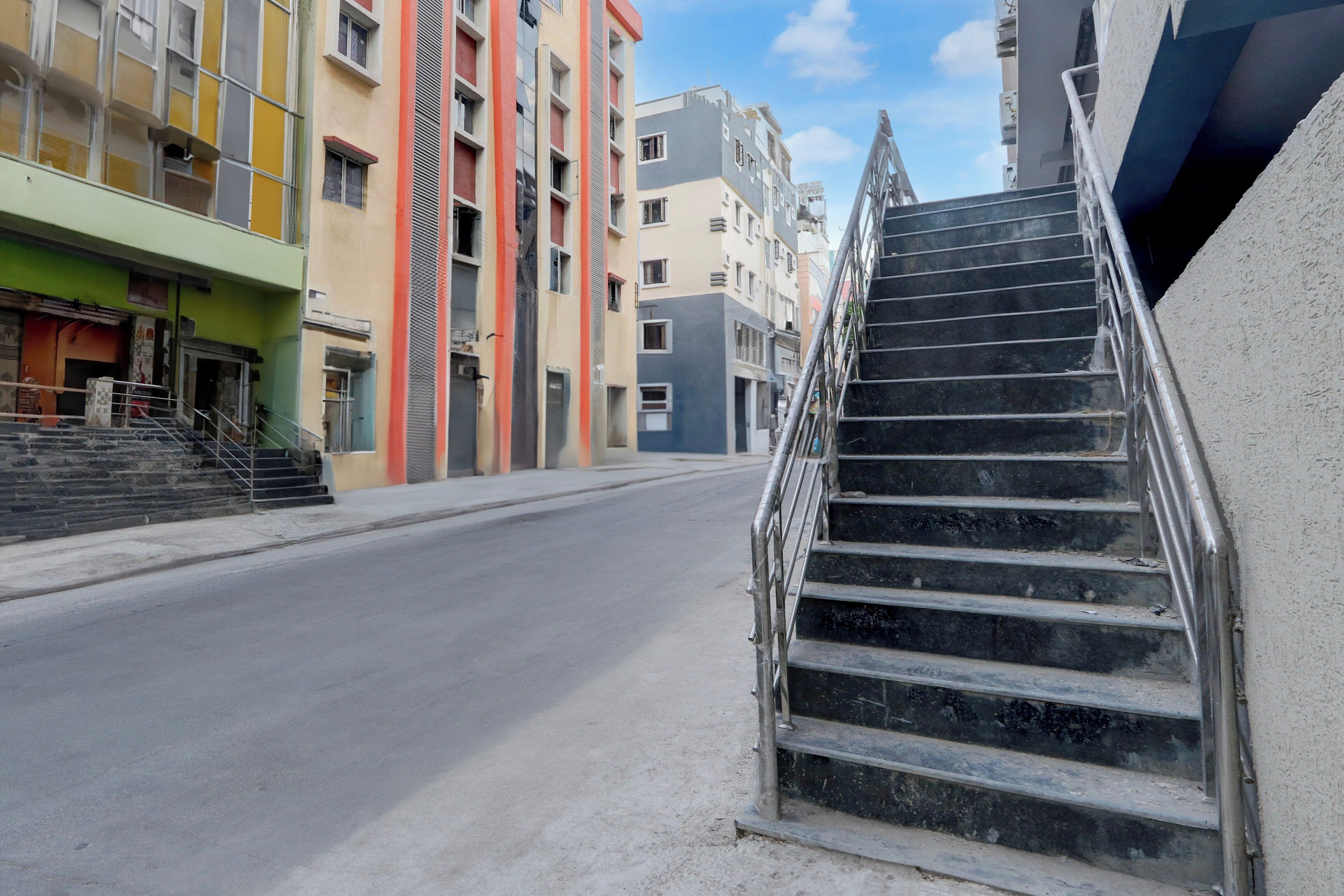 A staircase leading up to a building with multiple floors, a clear sky, and a street in the foreground.