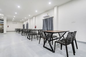A spacious indoor area with multiple tables and chairs, air conditioning units, and fire extinguishers. - Townhouse Shamshabad Near Airport (Hyderabad)