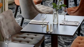 A dining area with round tables, grey upholstered chairs, and a vase with a yellow flower.