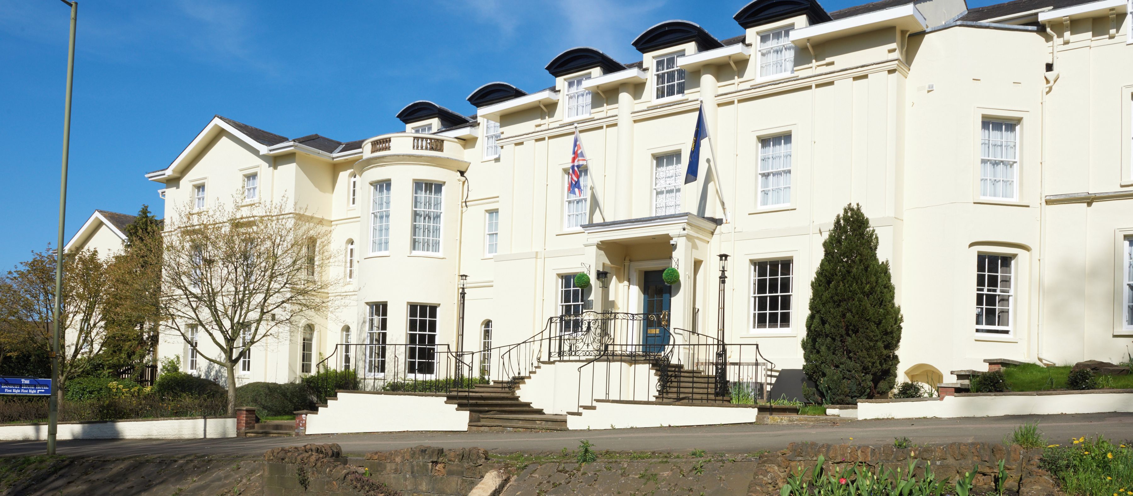 A multi-story hotel with a symmetrical facade, a central entrance with a staircase, and a flag on the roof.