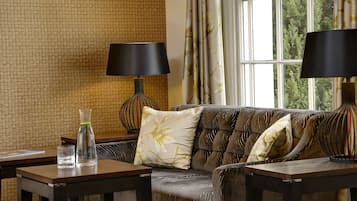 A living room with a sofa, two tables, a lamp, and a view of greenery through a window.
