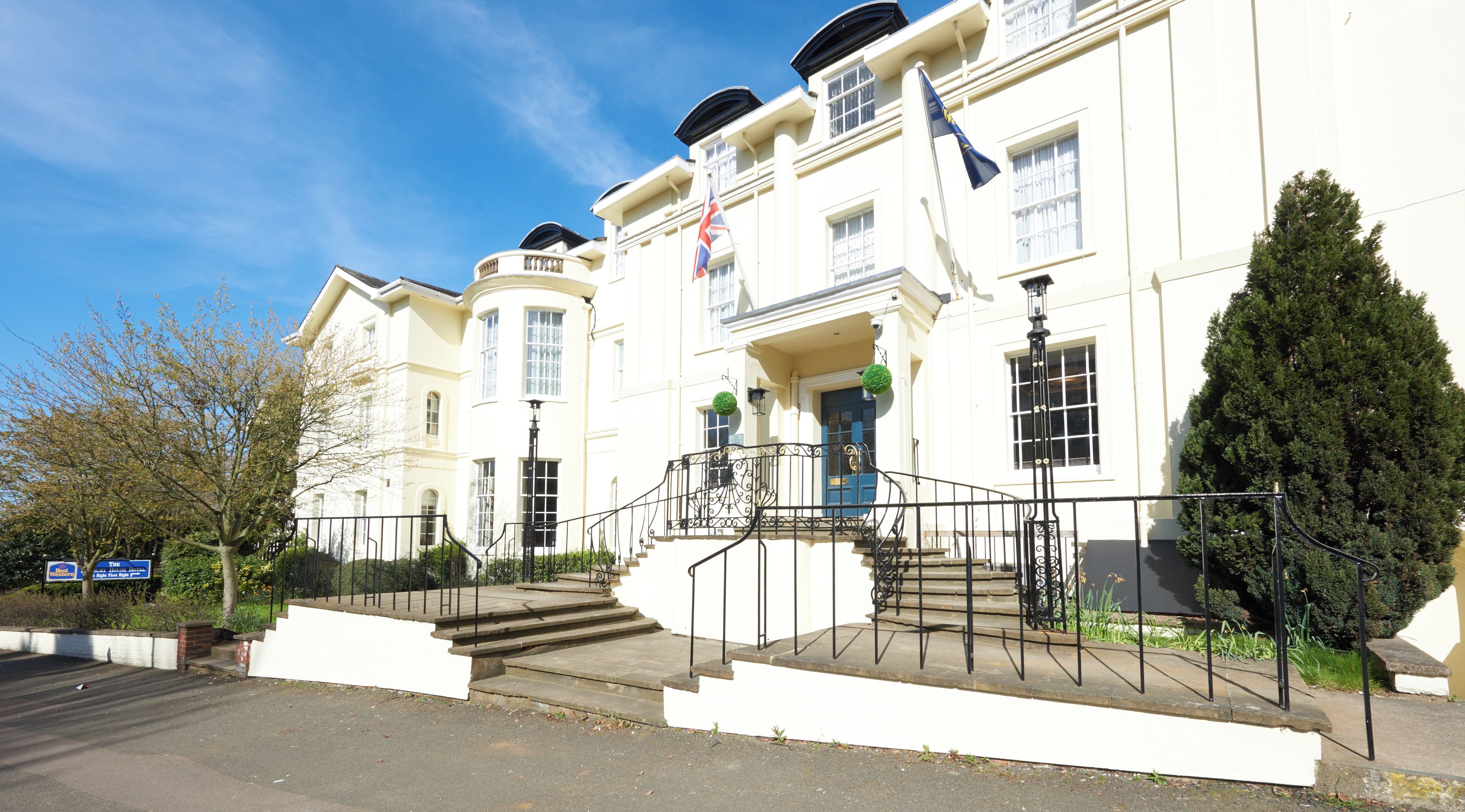 A white building with a blue door, a flag, and a staircase leading to the entrance.