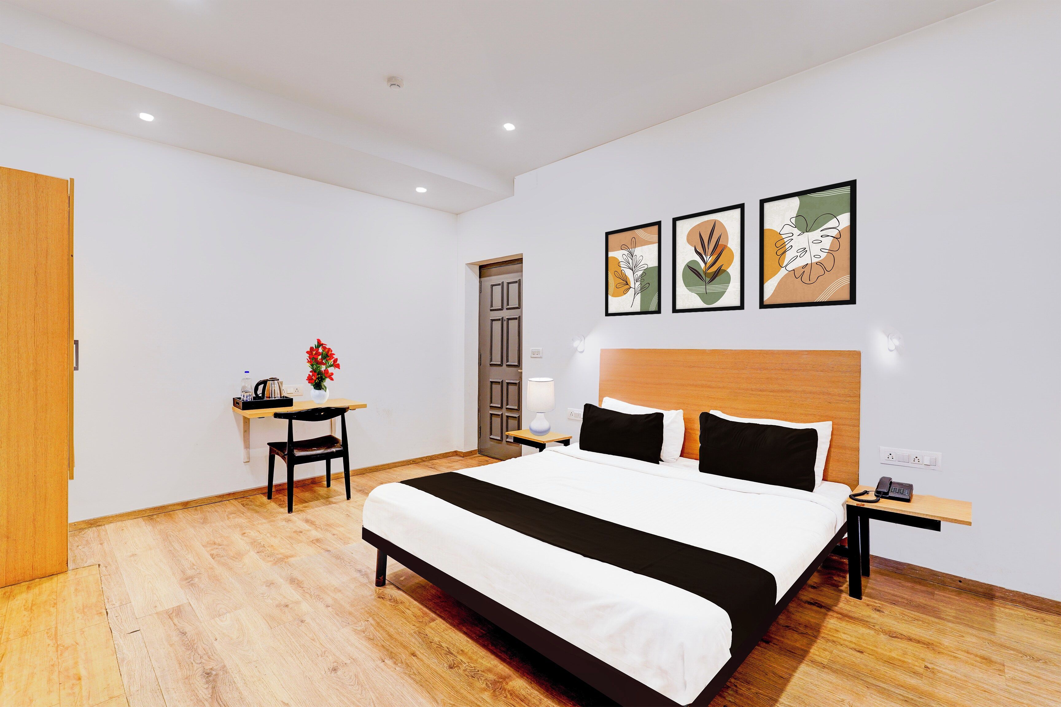 A hotel room with a large bed, a desk, a chair, a nightstand, and artwork on the wall.