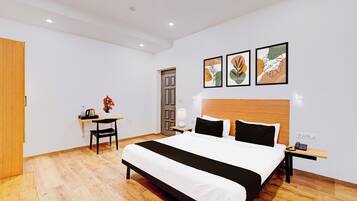 A hotel room with a large bed, a desk, a chair, a nightstand, and artwork on the wall.
