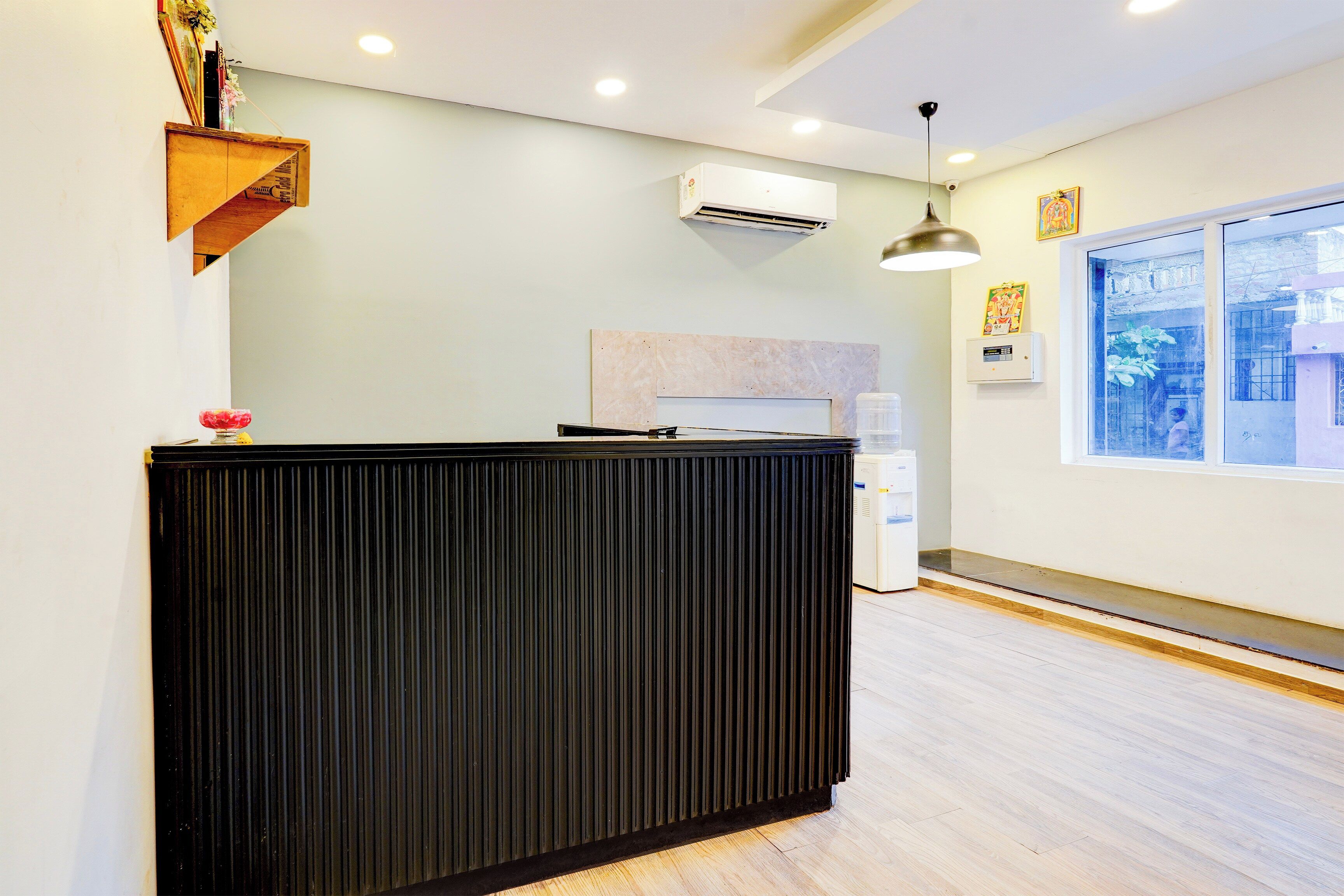 A reception desk with a modern design, an air conditioning unit mounted on the wall, and a window providing a view of the outside.