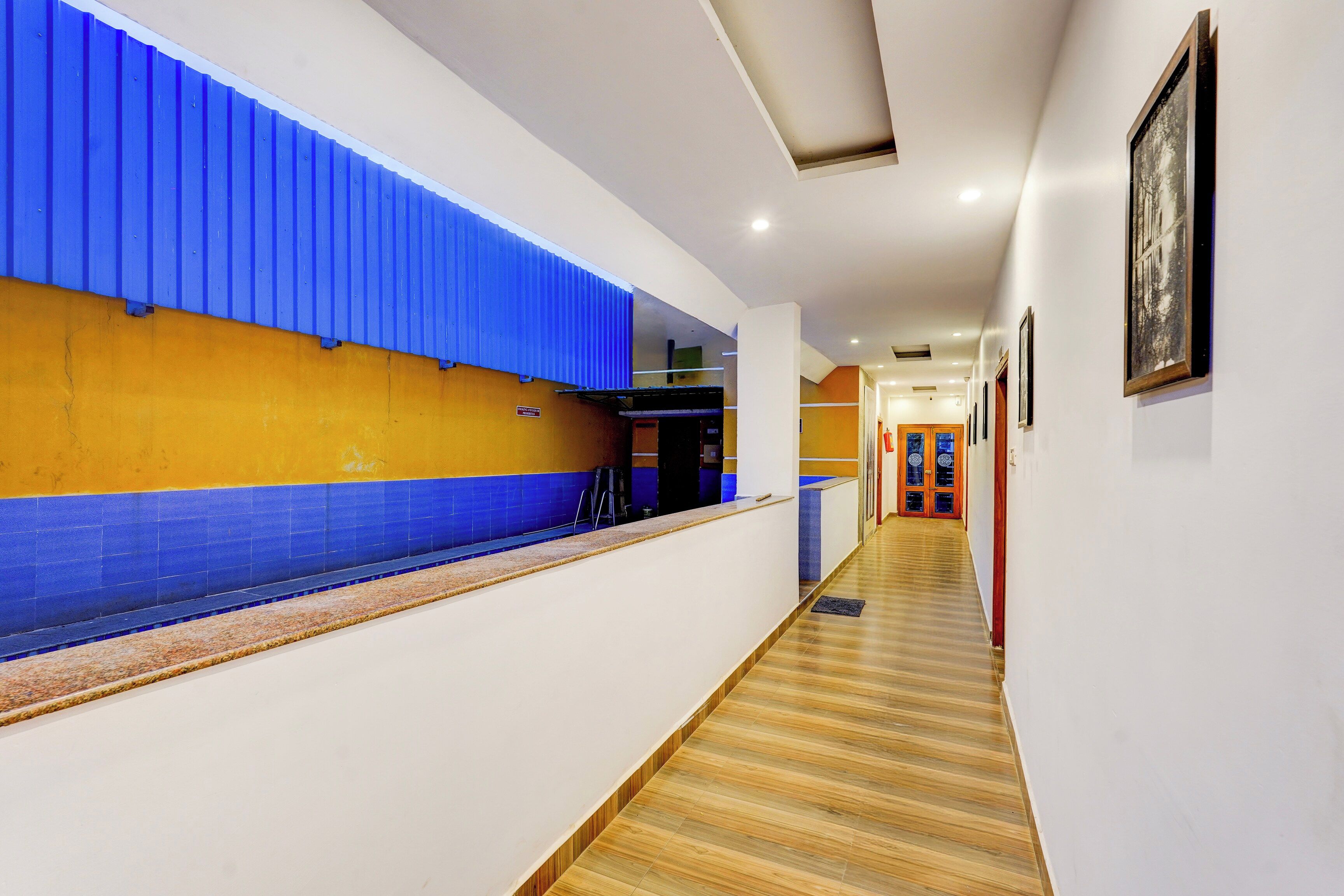 A hotel corridor with a reception desk, a blue and yellow wall, and a wooden floor.
