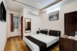 Una habitación de hotel con una cama, una mesita de noche, un espejo, una ventana con cortinas, un equipo de aire acondicionado y un cuadro en la pared.