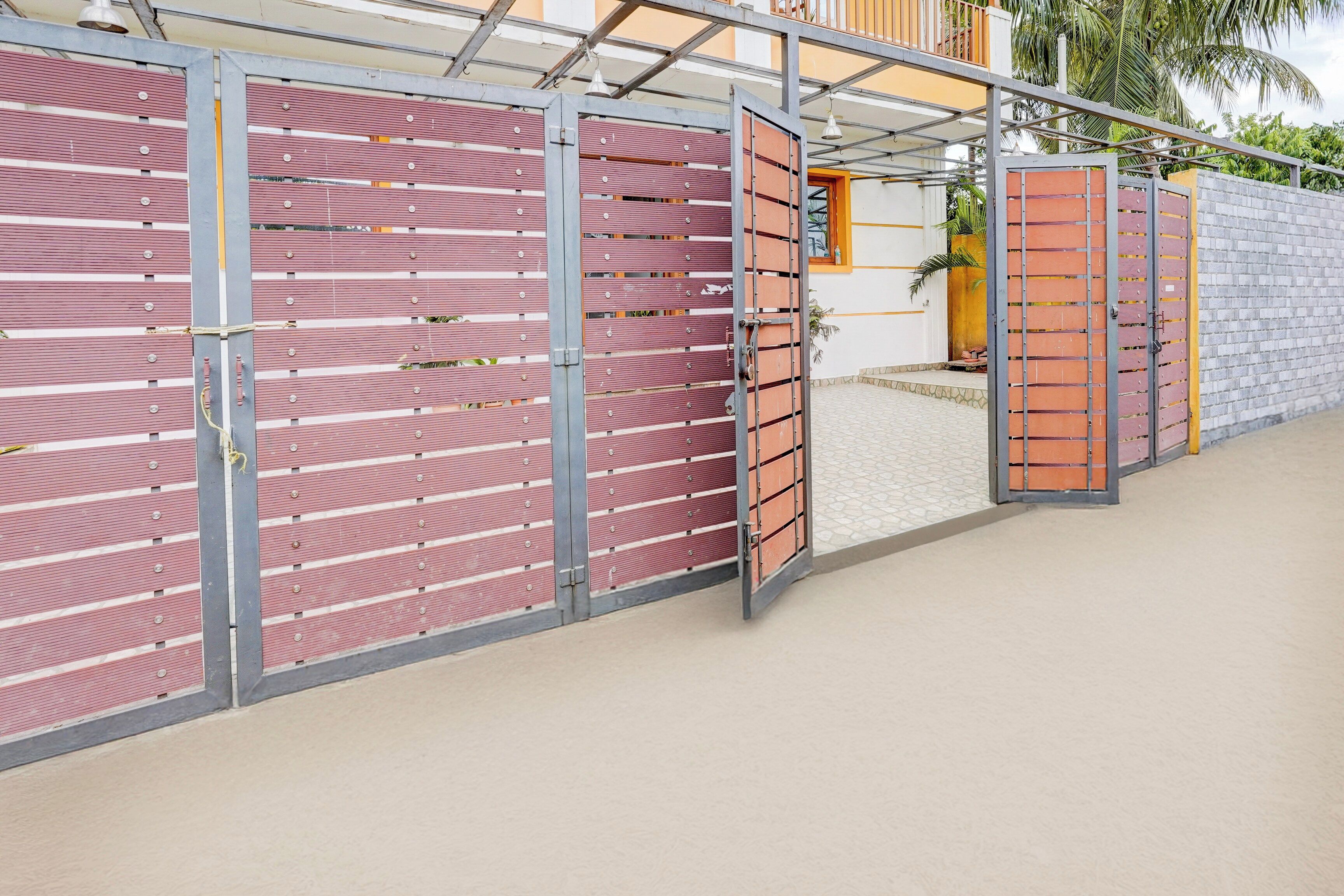 A gated entrance with multiple metal gates, a concrete pathway, and a building with a yellow and white facade.