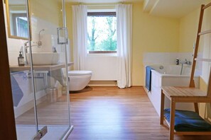 A bathroom with a glass shower enclosure, a toilet, a bathtub, and a window with curtains. - Beautiful from fishing (Saustrup)