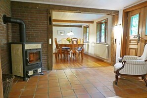 Ein rustikales Interieur mit Backsteinwand, Kaminofen, Essbereich mit Tisch und Stühlen sowie ein hölzerner Stuhl.