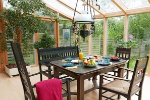 A conservatory with a dining table set for breakfast, surrounded by chairs and a hanging light fixture. - Beautiful from fishing (Saustrup)