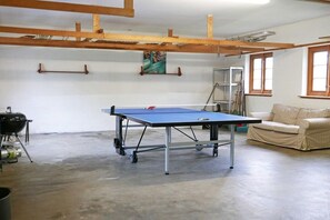 Ein Zimmer mit Tischtennisplatte, Grill und einer Couch.