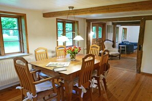 Un comedor con mesa y sillas de madera, un jarrón con flores y vistas al exterior a través de amplios ventanales.