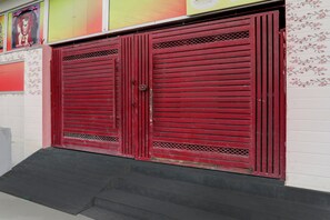 A red metal gate with a latch, set against a white wall with floral patterns. - Hotel O Saryu Ghat (Ayodhya)