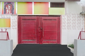 A red double door with a black mat in front, flanked by white walls with floral patterns. - Hotel O Saryu Ghat (Ayodhya)