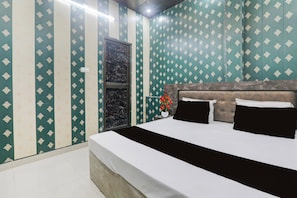 A bedroom with a bed, a nightstand, a vase with flowers, and a door with a marble pattern. - Hotel O Saryu Ghat (Ayodhya)