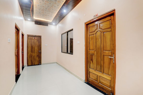 A hallway with wooden doors, a tiled floor, and a ceiling with a patterned design. - Hotel O Saryu Ghat (Ayodhya)