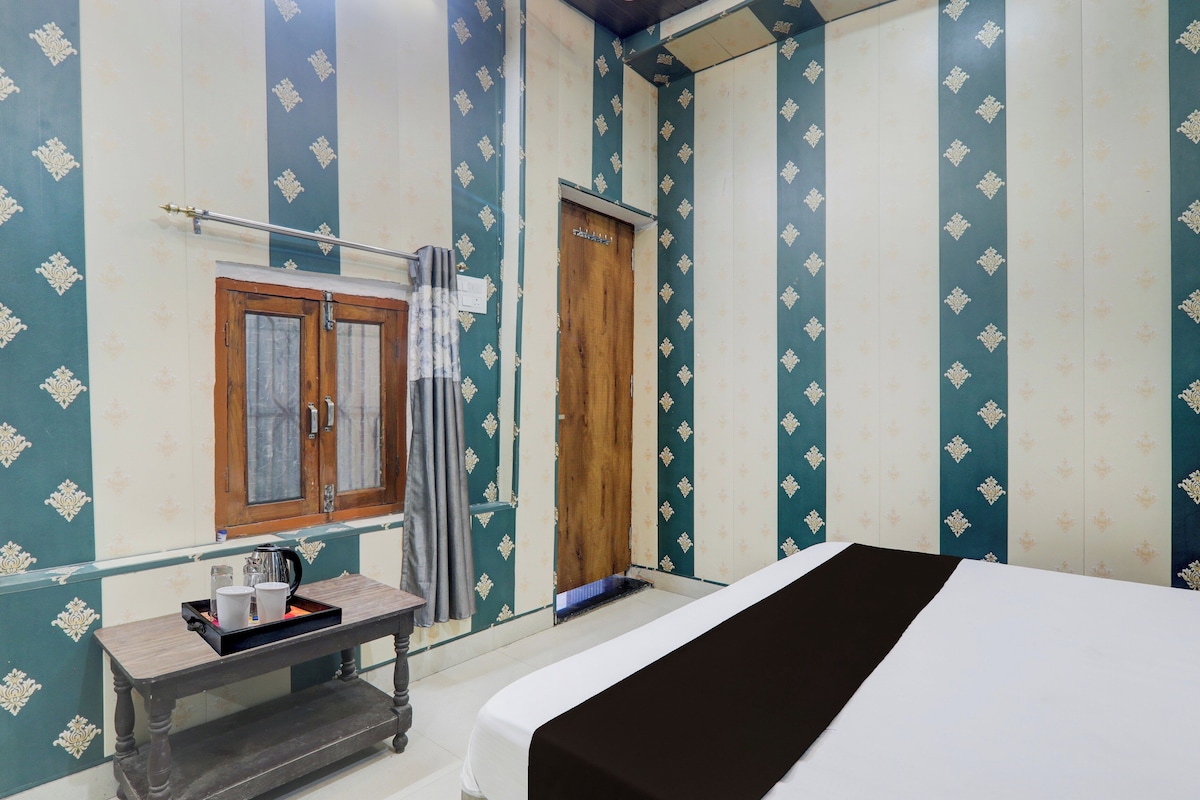 A room with a bed, a wooden wardrobe, a small table with a kettle, and a curtain.