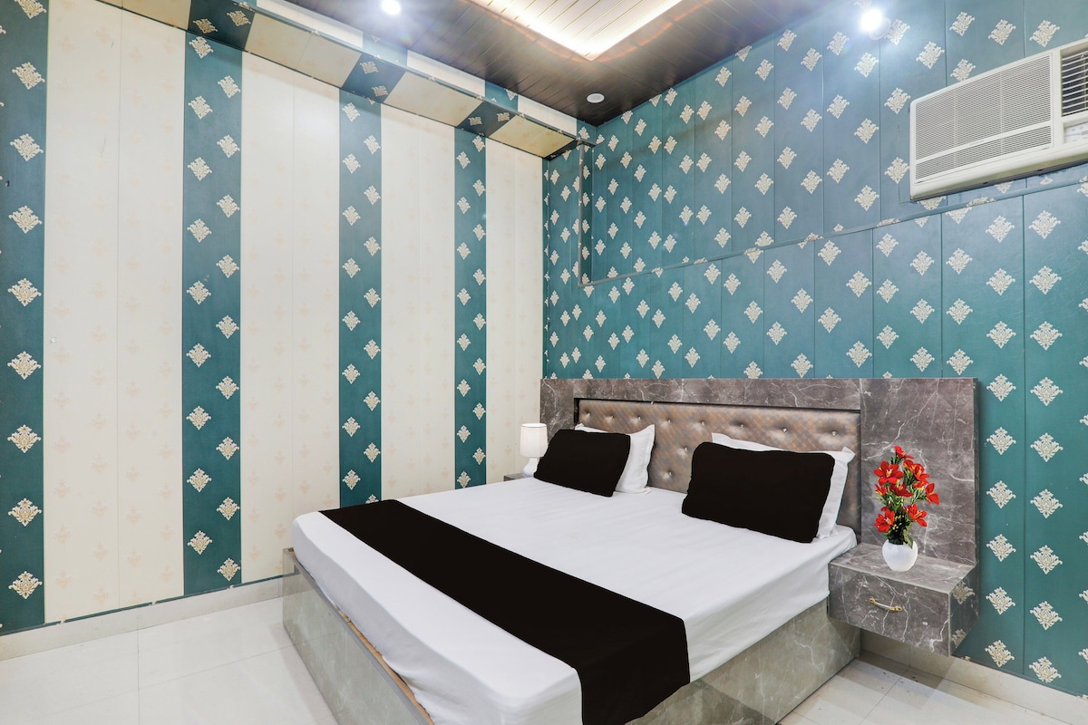 A hotel room with a bed, nightstand, and a wall-mounted air conditioner.