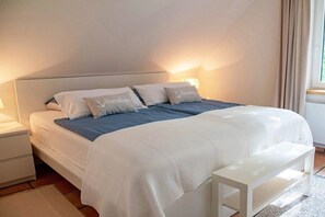 Ein ordentlich bezogenes Bett mit einem weißen Kopfteil, zwei Kissen mit Aufdruck, einer blauen Decke und einem weißen Nachttisch.