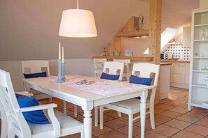 Ein Essbereich mit einem weißen Tisch und Stühlen, einer Pendelleuchte und einer Küche im Hintergrund.