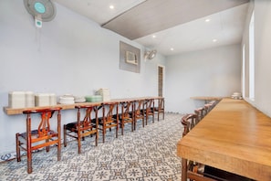Una sala de conferències amb una taula de fusta llarga, diverses cadires i una pila de plats blancs a la paret.