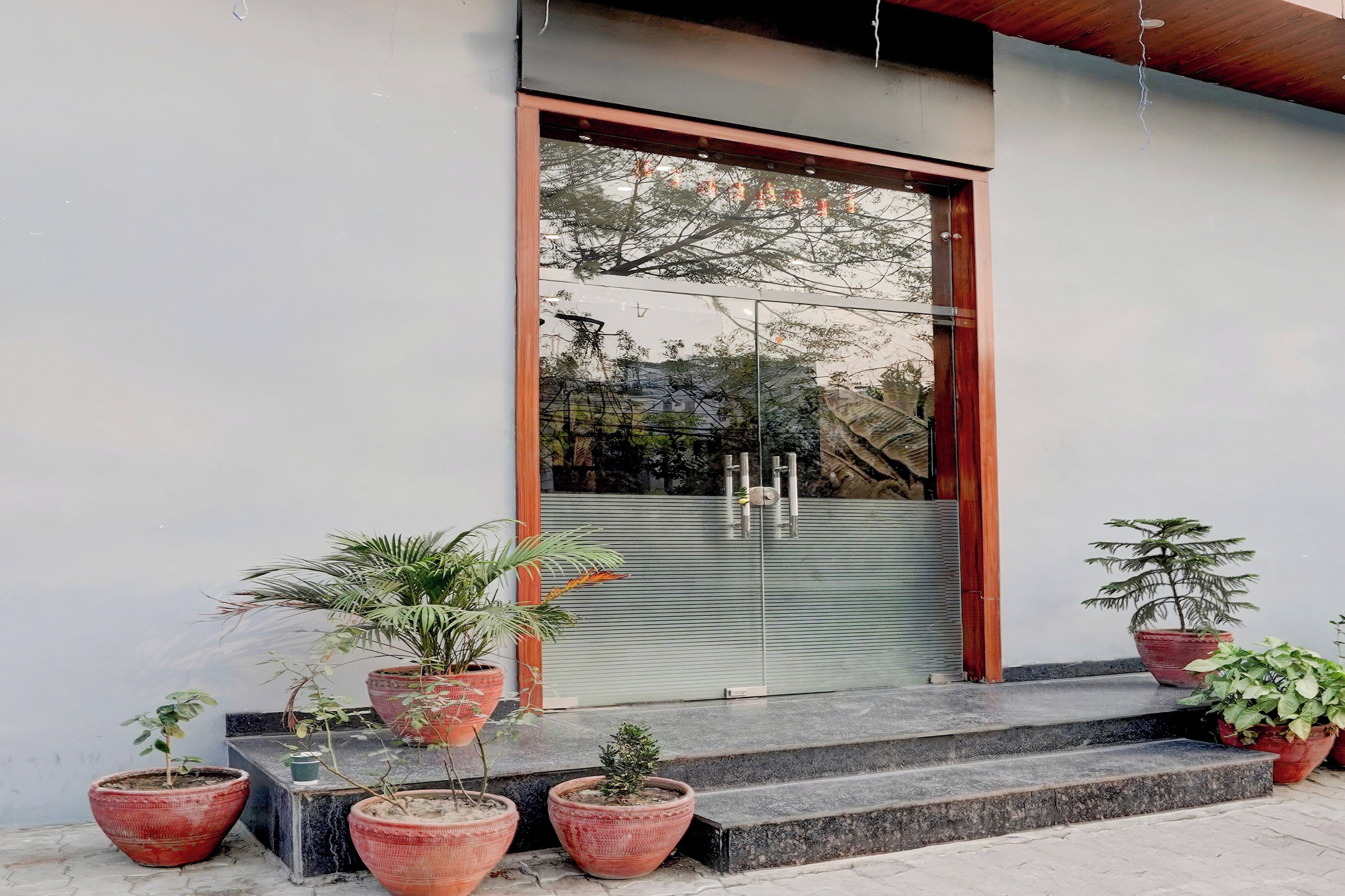 A modern building entrance with a glass door, potted plants, and a metal staircase.