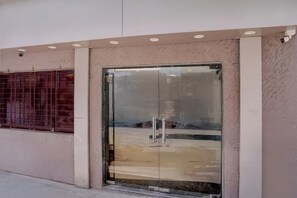 Entrada de um edifício com porta de vidro e portão de segurança metálico.