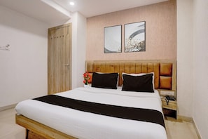 Habitación de hotel con estructura de cama de madera, cubrecama blanco, dos almohadas negras, mesita de noche de madera con teléfono y dos obras de arte colgadas en la pared.