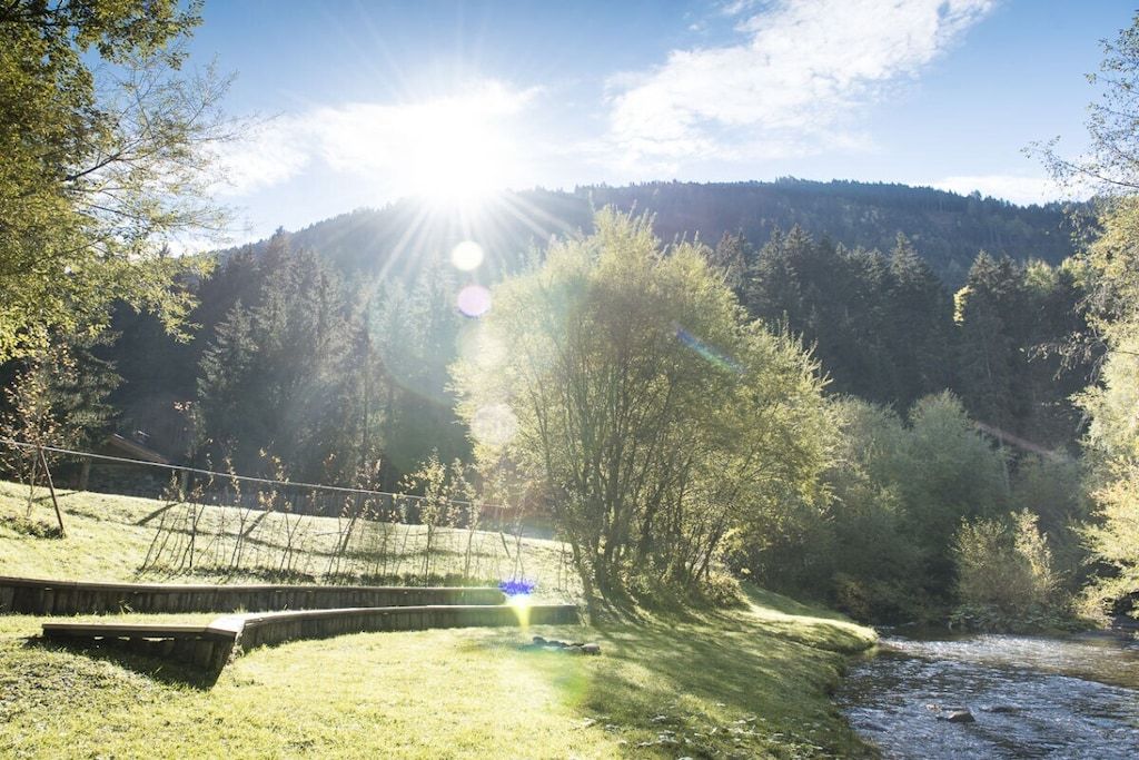 Een rivier die door een bebost gebied stroomt, met een houten brug en een heldere lucht.