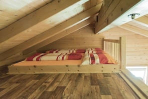 A loft bedroom with a wooden sloped ceiling, a bed with striped bedding, and a wooden floor. - Holiday home in Rangersdorf with barbecue (Rangersdorf)