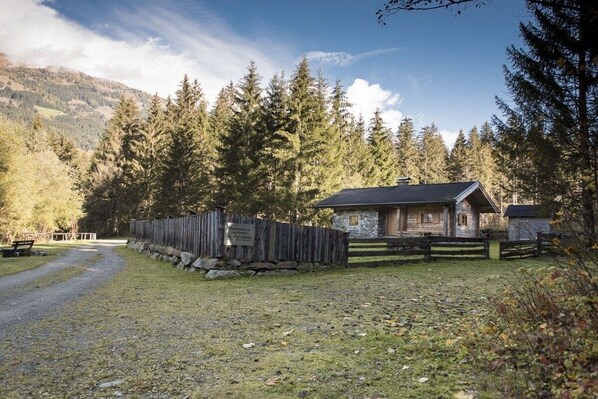 A cabin with a stone exterior, surrounded by a wooden fence, set in a forested area with a gravel path leading to it. - Holiday home in Rangersdorf with barbecue (Rangersdorf)