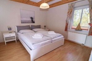 Ein Schlafzimmer mit einem Bett, Nachttischen, einem Fenster mit Vorhängen und einer Deckenleuchte.