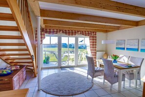 Ein Zimmer mit einer Treppe, einem Essbereich mit Korbstühlen, einem Tisch und Blick durch eine Glastür.