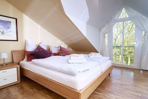 A bedroom with a wooden bed, white bedding, and a window with a view of trees. - Holiday apartment with 2 bedrooms (Kopperby)