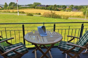 Eine Terrasse mit einem runden Tisch und zwei Stühlen, mit Blick auf ein Wiesenfeld und Häuser in der Ferne.