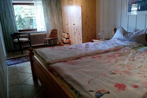 A bedroom with two beds, a chair, a radiator, and a window with curtains. - Holiday apartment in Heikendorf with Wi-Fi (Heikendorf)
