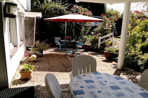 A patio with a table and chairs, surrounded by potted plants and a red umbrella. - Holiday apartment in Heikendorf with Wi-Fi (Heikendorf)