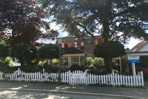 A building with a white picket fence, surrounded by trees and flags. - Holiday apartment in Heikendorf with Wi-Fi (Heikendorf)