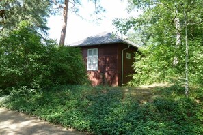 A small, single-story building with a sloped roof, surrounded by dense greenery. - Holiday apartment with 1 bedroom (Caputh)