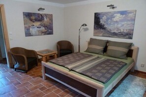A bedroom with a bed, two chairs, a small table, and two paintings on the wall. - Holiday apartment with 1 bedroom (Caputh)