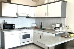 A compact kitchen with white cabinets, a microwave, a stove, a coffee maker, and a small potted plant. - Anchorage 9, House Baltic (Sellin)
