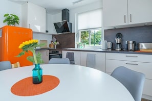 A modern kitchen with white cabinets, a built-in oven, a coffee maker, and a window with blinds. - Holiday home with 1 bedroom (Boiensdorf OT Stove)