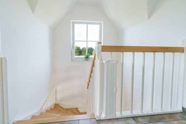 Una escalera con barandilla blanca, una ventana con vistas a follaje y un pasamanos de madera.