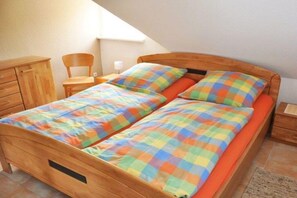 A single bed with a colorful checkered bedspread and matching pillows, a wooden nightstand, a chair, and a small wooden dresser. - Holiday home with 1 bedroom (Kaltenhof (Insel Poel))
