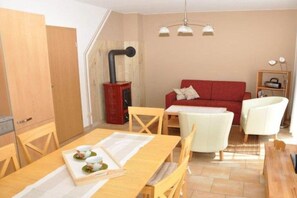 A cozy living room with a red sofa, a dining table with chairs, and a kitchen area with cabinets. - Holiday home with 1 bedroom (Kaltenhof (Insel Poel))